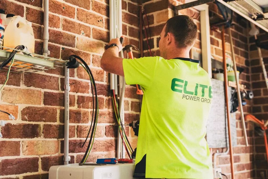 An electrician in a hi-vis shirt wiring a brick wall in a garage
