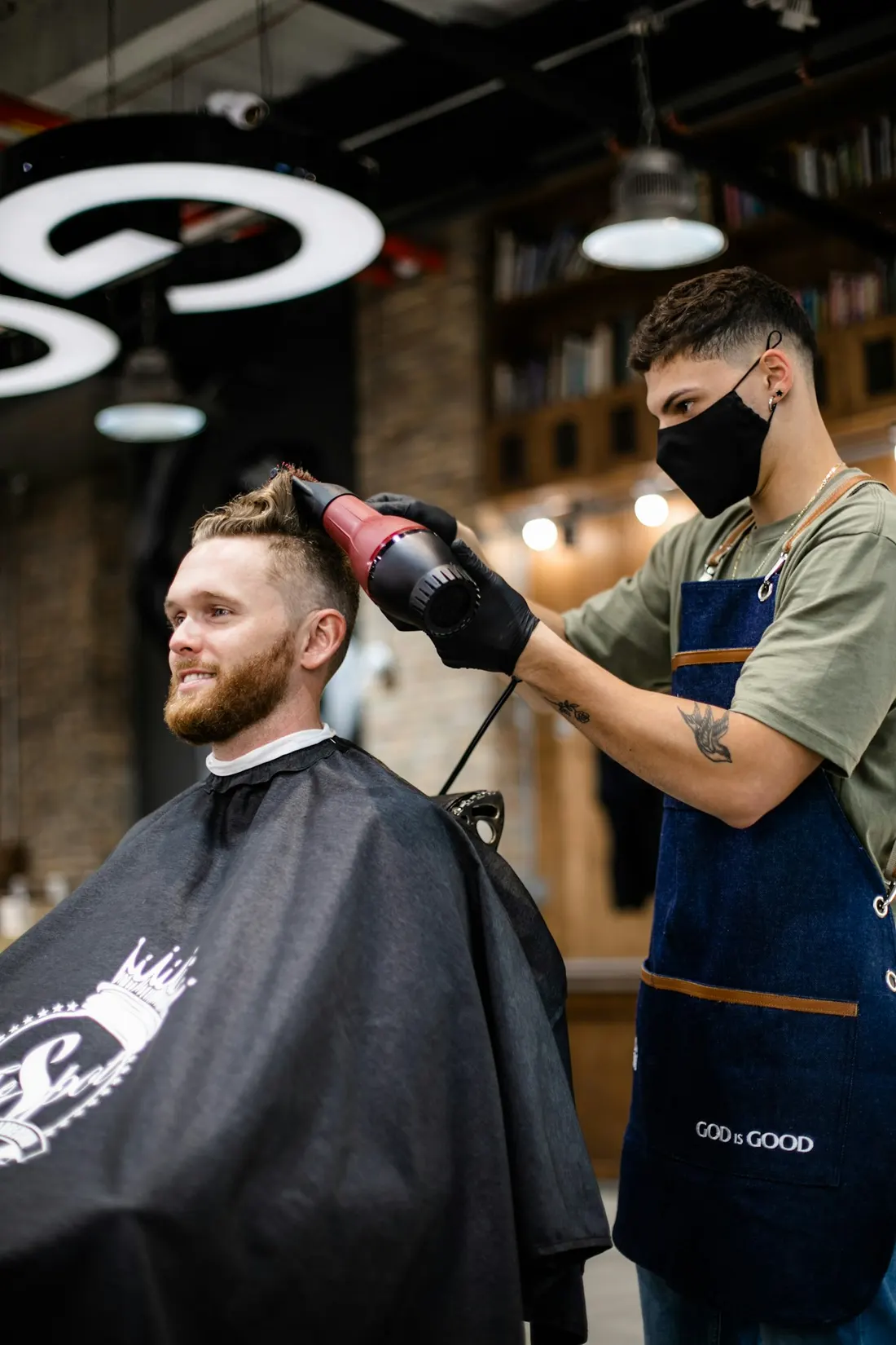 A barber blow-drying a client's hair in his shop